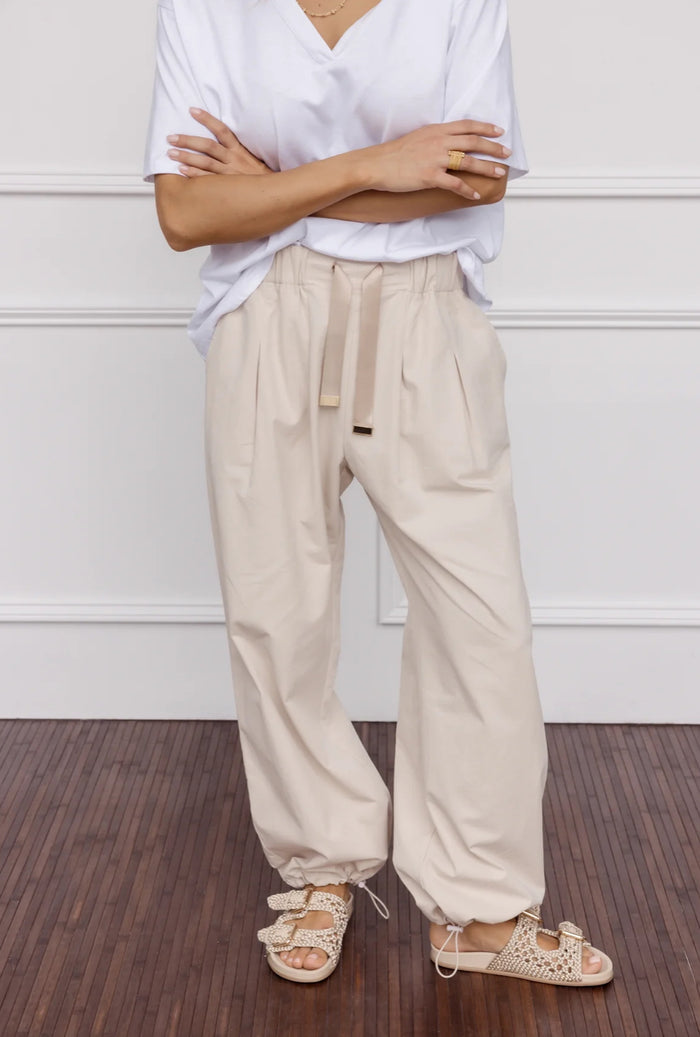 Person wearing a white shirt and beige pants standing against a white wall.
