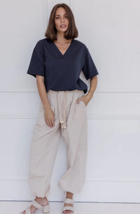Woman wearing a navy blue top and beige pants against a white background