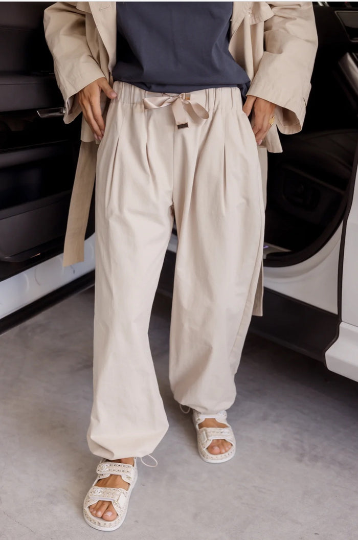 Person wearing a beige trench coat and pants with white sandals in an indoor setting.