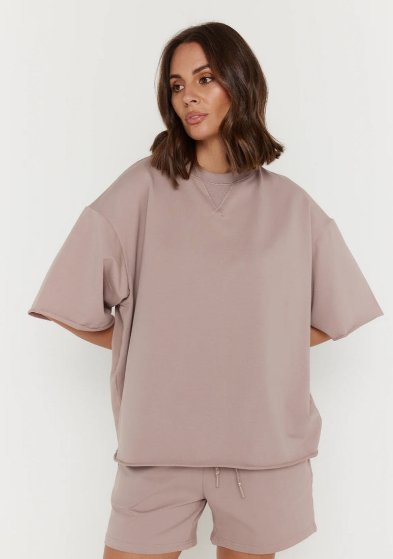Woman wearing a beige oversized sweatshirt and shorts set on a white background
