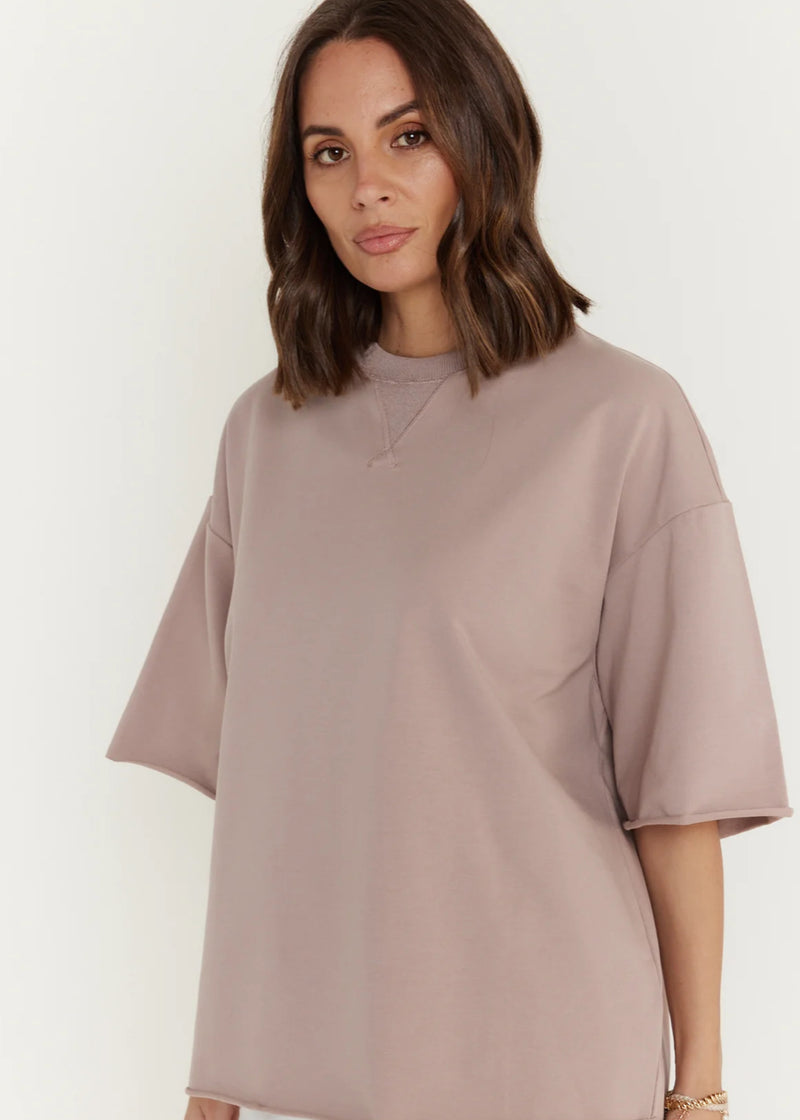 Woman wearing a light brown oversized t-shirt against a white background