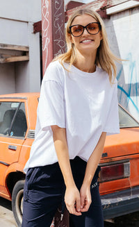 Woman wearing a white t-shirt and sunglasses standing in front of an orange car.
