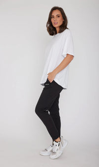 Woman wearing a white t-shirt and black pants on a plain background