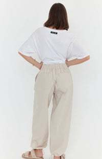 Person wearing a white oversized t-shirt and beige pants on a plain background
