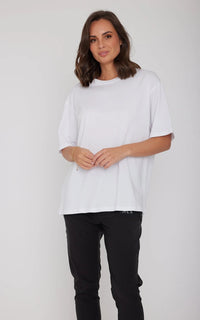 Woman wearing a white oversized t-shirt and black pants on a plain background