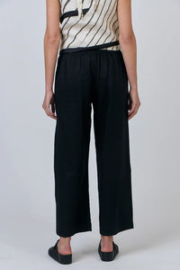 Person wearing black wide-leg pants and a patterned top on a plain background