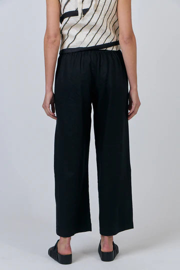 Person wearing black wide-leg pants and a patterned top on a plain background
