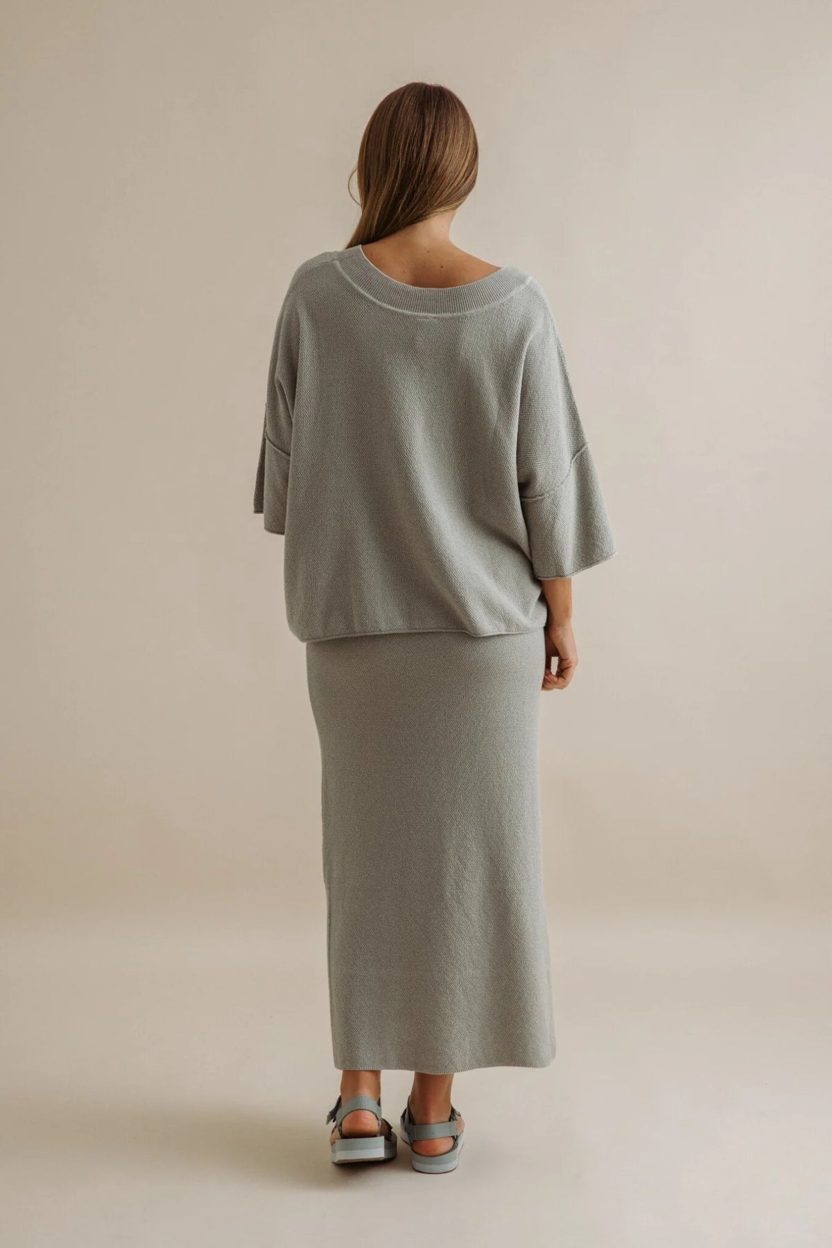 Woman wearing a gray outfit standing against a beige background