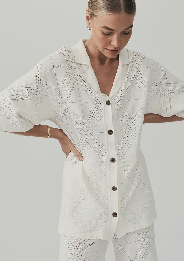 Woman wearing a white embroidered blouse with buttons on a plain background