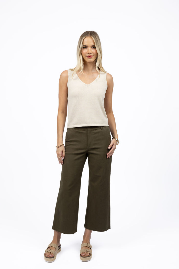 Woman wearing a beige sleeveless top and brown pants on a white background