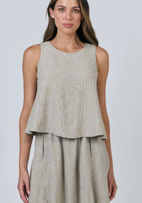 Woman wearing a sleeveless beige top and matching skirt on a plain background