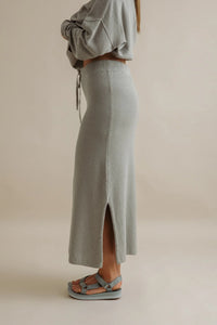 Person wearing a light gray knit skirt with a plain background
