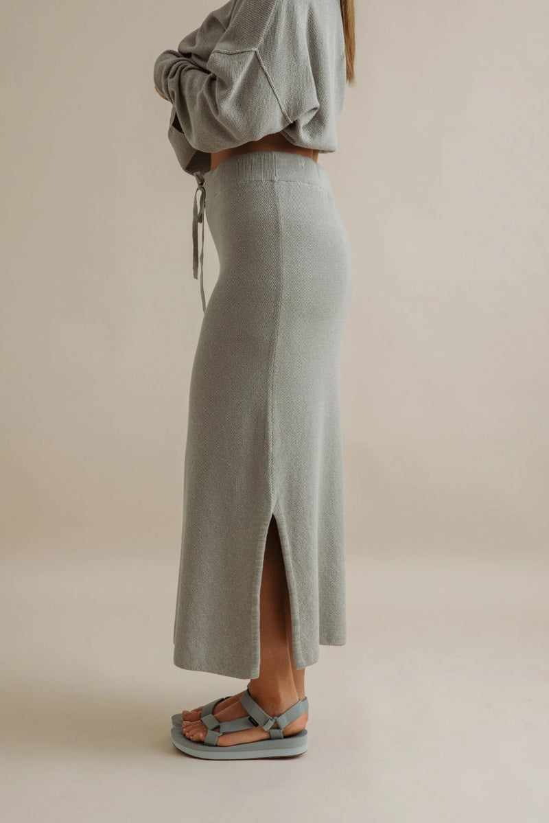 Person wearing a light gray knit skirt with a plain background