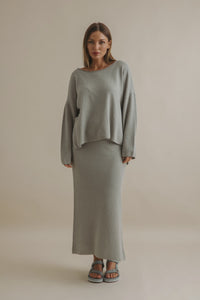 Woman wearing a gray sweater and skirt set against a beige background