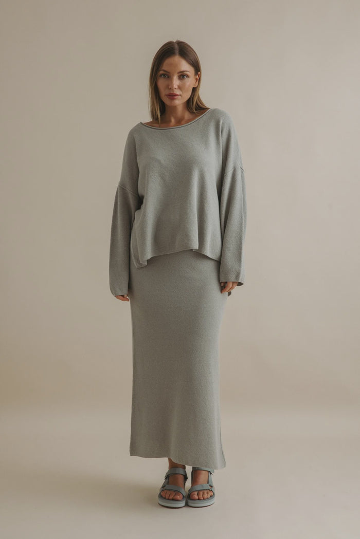 Woman wearing a gray sweater and skirt set against a beige background