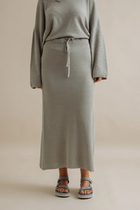 Person wearing a gray outfit with a long skirt on a beige background