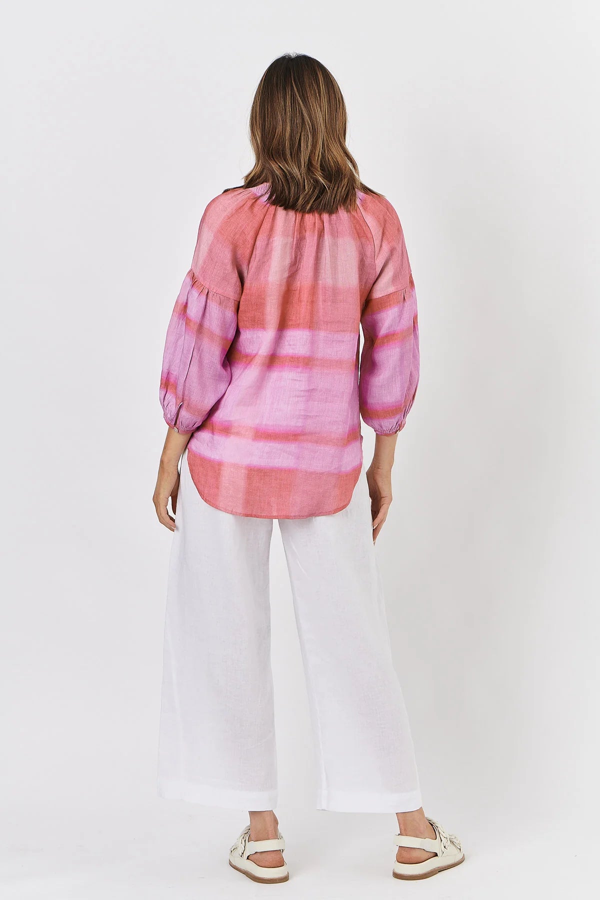 Person wearing a pink and purple striped shirt with white pants on a white background