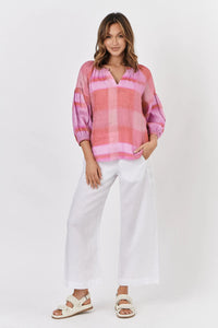 Woman wearing a pink plaid blouse and white pants on a white background