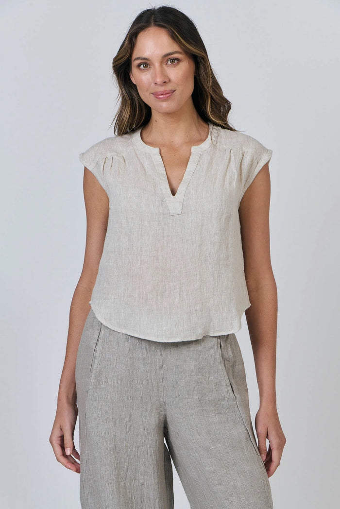 Woman wearing a light-colored sleeveless top and gray pants against a plain background