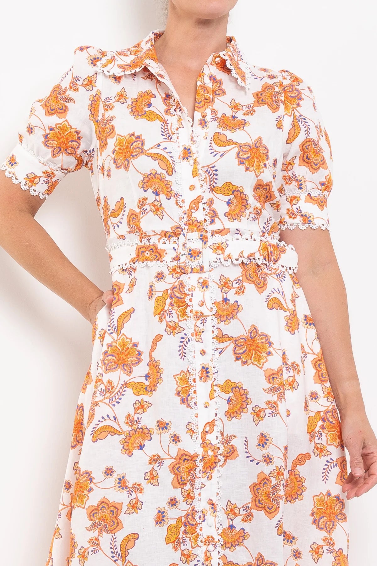 Woman wearing a white dress with orange floral pattern on a plain background