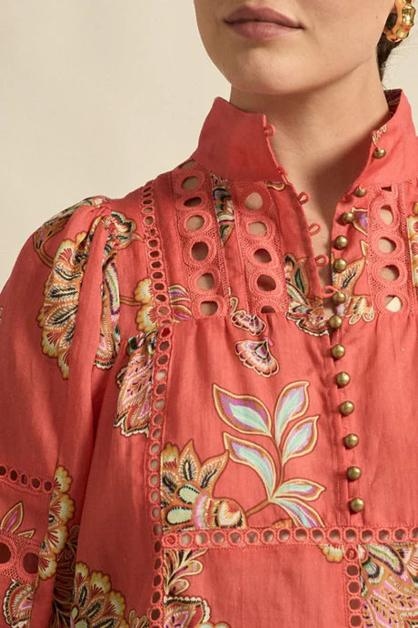 Close-up of a person wearing a coral pink embroidered blouse with floral patterns.