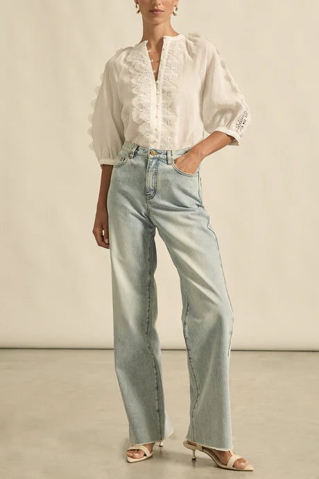 Person wearing a white blouse and light blue jeans against a neutral background