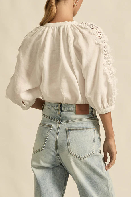 Person wearing a white blouse with embroidery and light blue jeans on a beige background