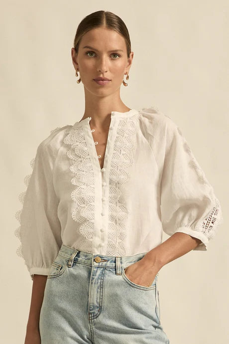 Woman wearing a white blouse with lace details and light blue jeans against a beige background