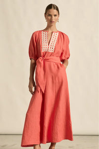 Woman wearing a coral dress with lace detailing on a beige background