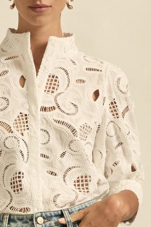 Close-up of a person wearing a white lace top with cut-out patterns.