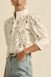 Person wearing a white lace blouse with long sleeves and light blue jeans on a beige background
