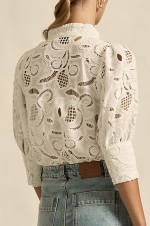 Person wearing a beige lace top with a neutral background