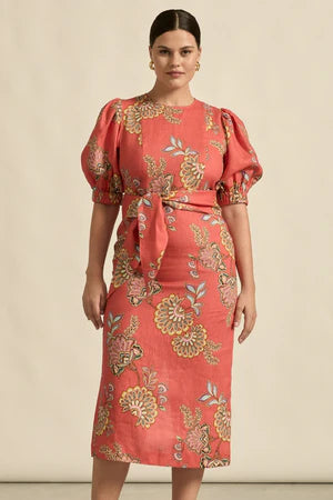 Woman wearing a coral dress with gold floral patterns against a beige background