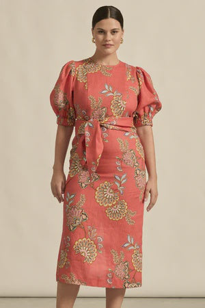 Woman wearing a coral dress with floral pattern against a beige background