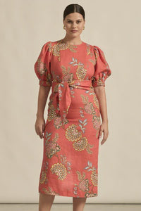 Woman wearing a coral dress with floral pattern against a beige background